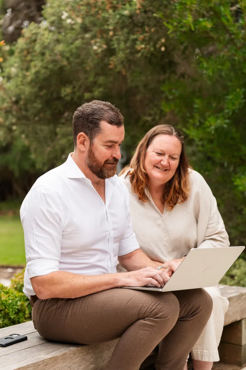Two people on a garden bench looking at a laptop together