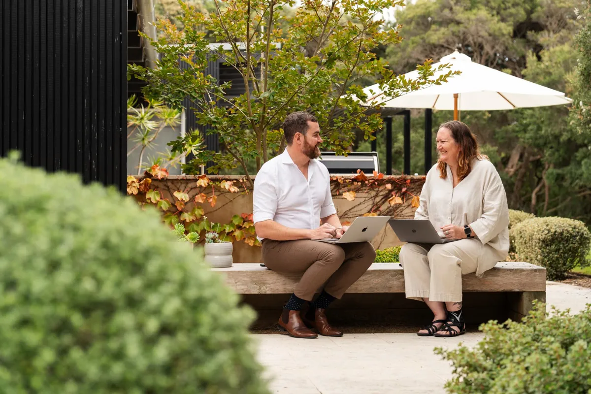 Two Future Finance Group team members working on laptops on a long timber garden bench